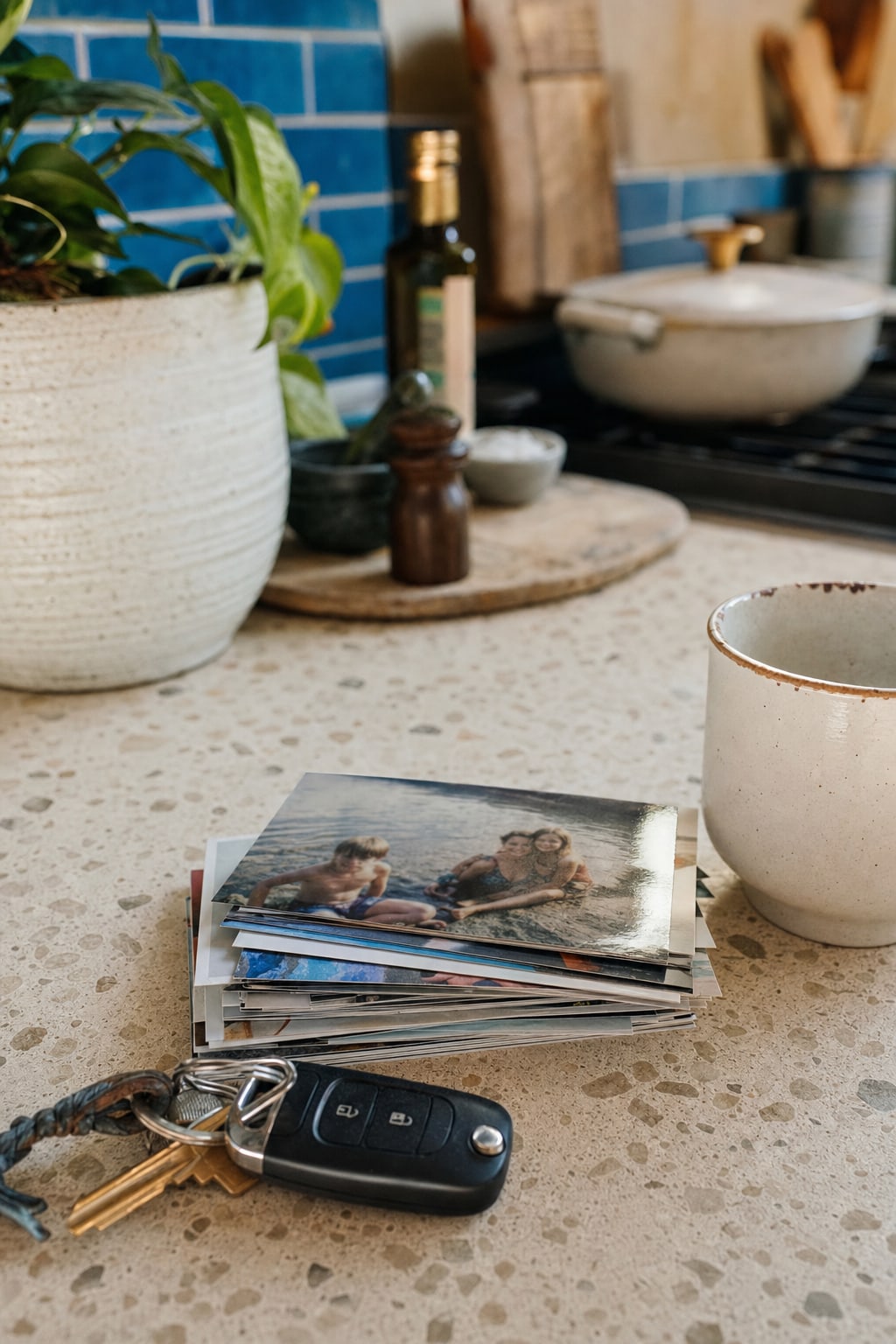 A stack of photo prints on a kitchen counter beside keys and a mug